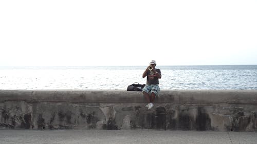 Man Playing A Trumpet While Sitting On The Seawall