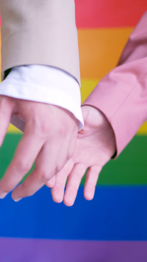 Close up of People Holding Hands in Front of a Gay Pride Flag