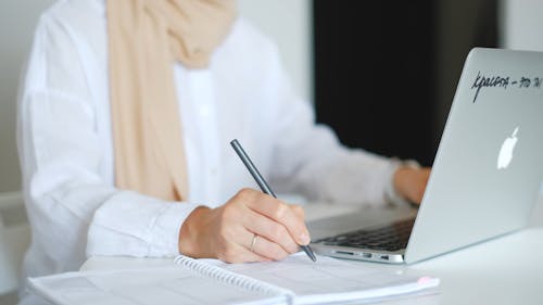 Person With a Laptop and Taking Notes