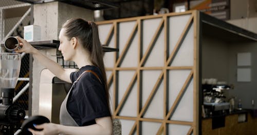 A Female Barista Grounding Coffee Beans On A Machine