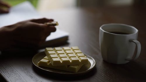 A Person Writing On The Table With White Chocolate Bars And A Drink