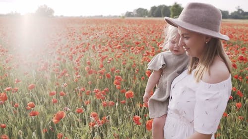 Woman Walking on Red Poppy Flower Field While Carrying Her Baby