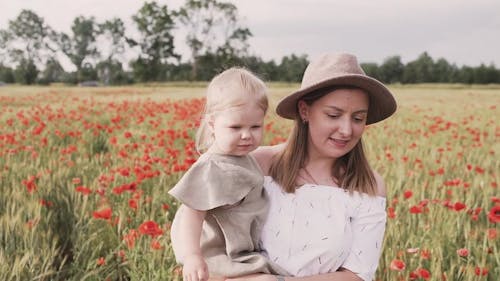 Woman Walking on Red Poppy Flower Field While Carrying Her Baby