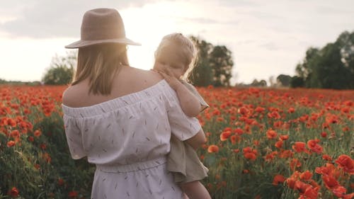 Woman Walking on Red Poppy Flower Field While Carrying Her Baby