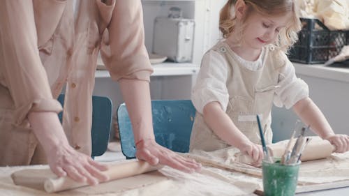 A Mother And Daughter Flattening Dough With Rolling Pins