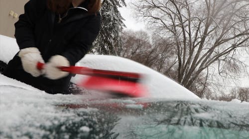 Close-Up View of Person Brushing Off Snow From Her Car