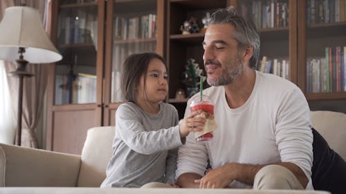 Daughter Holding the Beverage for Her Dad to Drink