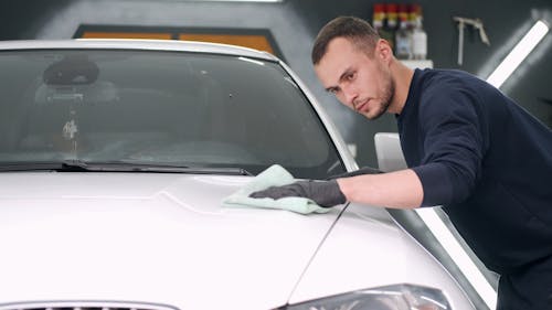 Man Wiping the White Car Hood Using Cloth