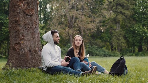 Man and Woman Sitting by the Tree Trunk While Talking to Each Other