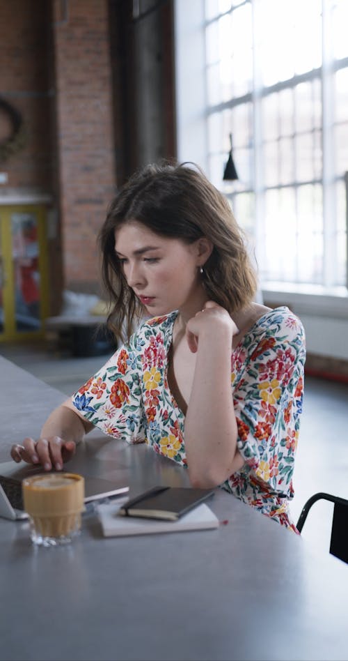 Женщина в рубашке с цветочным рисунком, используя ноутбук, попивая кофе