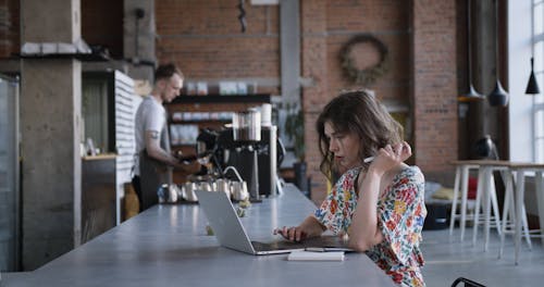 남자가 그녀의 커피를 제공하는 동안 그녀의 노트북을 사용하는 꽃 셔츠에 여자