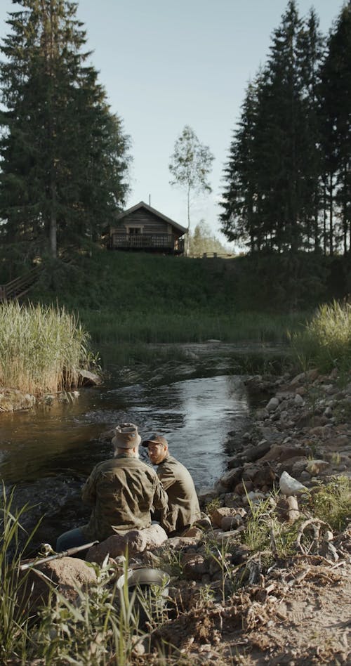 Two Men Sitting by the River Bank While Talking to Each Other