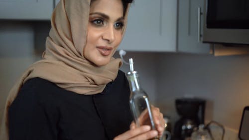 A Woman Talking and Holding a Bottle of Olive Oil