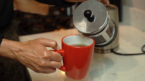 Person Pouring Tea in a Red Mug