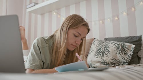 Woman Lying on Bed Writing on Her Notebook