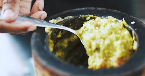 Close-Up View of a Person Transferring a Guacamole into a Bowl