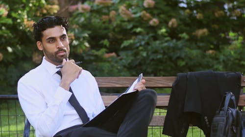 A Man Writing While Seated On A Wooden Bench