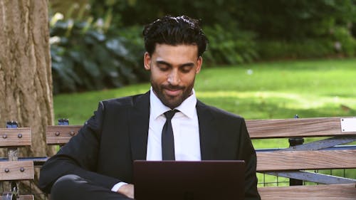Man Sitting on a Park Bench while Using His Laptop
