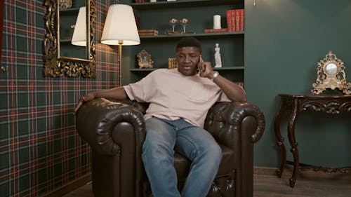 Man Sitting on Chair while Talking on Cellphone