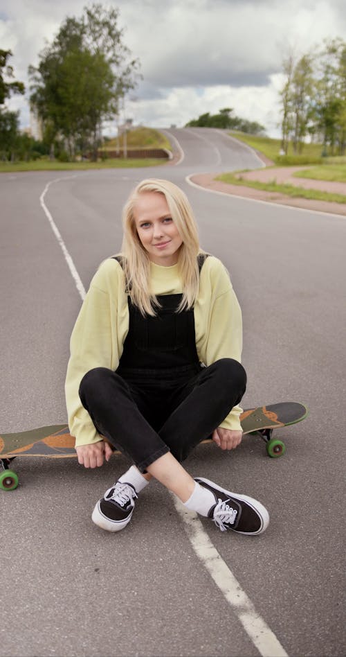 Young Woman Sitting on a Longboard at the Street