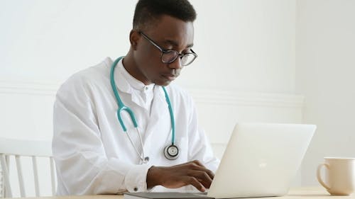 Man in White Lab Coat Using a Laptop