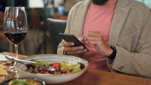 A Man Drinking Wine while Using His Phone