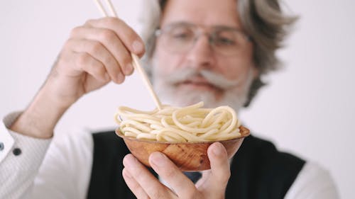 Close-Up View of a Man Holding a Bowl of Noodles