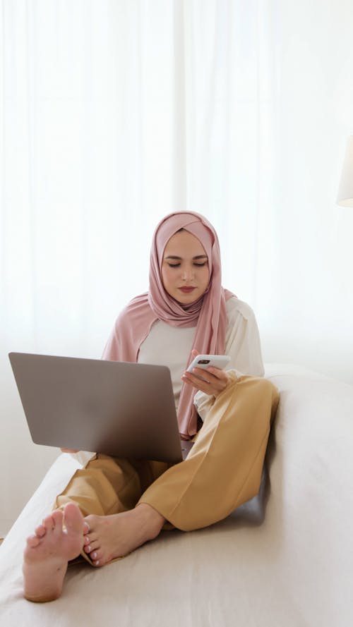 Woman in Pink Hijab Sitting on White Sofa While Having a Phone Call