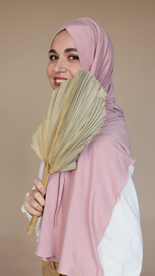 Woman in Pink Hijab Smiling While Holding a Leaf