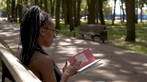 A Woman Reading A Book On The Park Bench