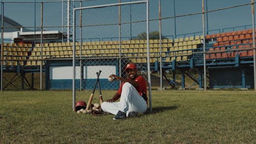 Baseball Player Sitting on Baseball Field While Holding a Baseball
