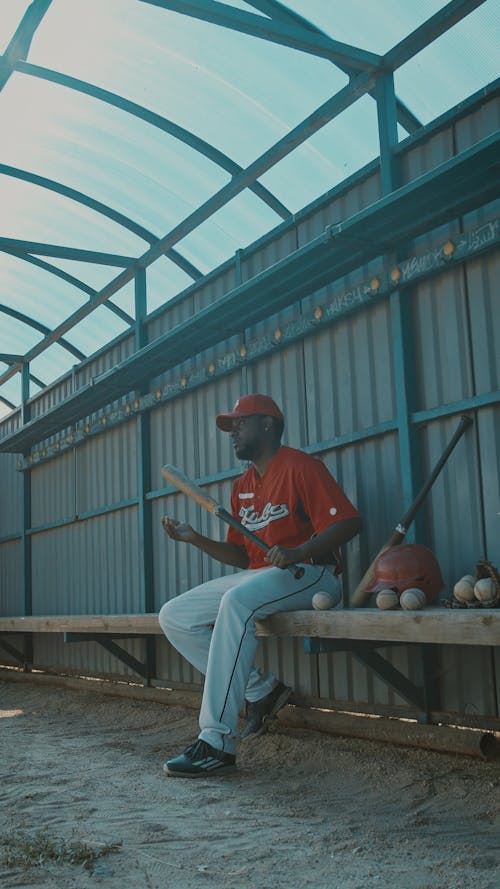 Baseball Player Sitting on a Bench While Holding His Baseball Bat