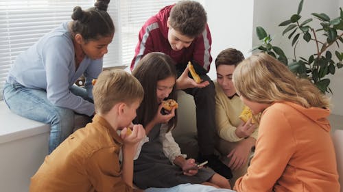 Teenagers Looking at the Smartphone While Eating Pizza