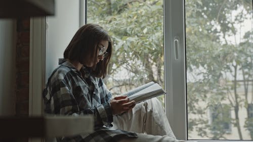 Woman Sitting by the Table While Reading a Bible