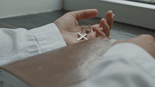 Close-Up View of a Person Holding a Silver Cross Pendant and Bible