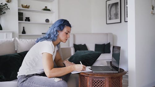 Woman Writing on Paper while Looking at Laptop
