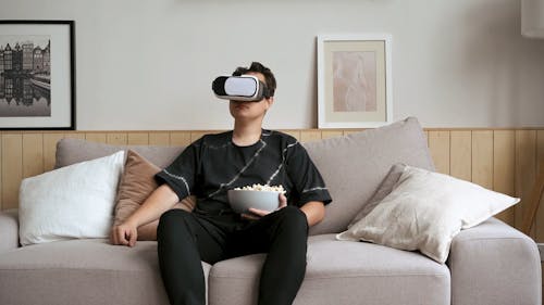 Man Using a Virtual Reality Box on the Sofa While Having Popcorn