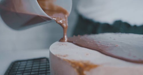 A Person Pouring Chocolate Syrup on the Ice Cream Cake