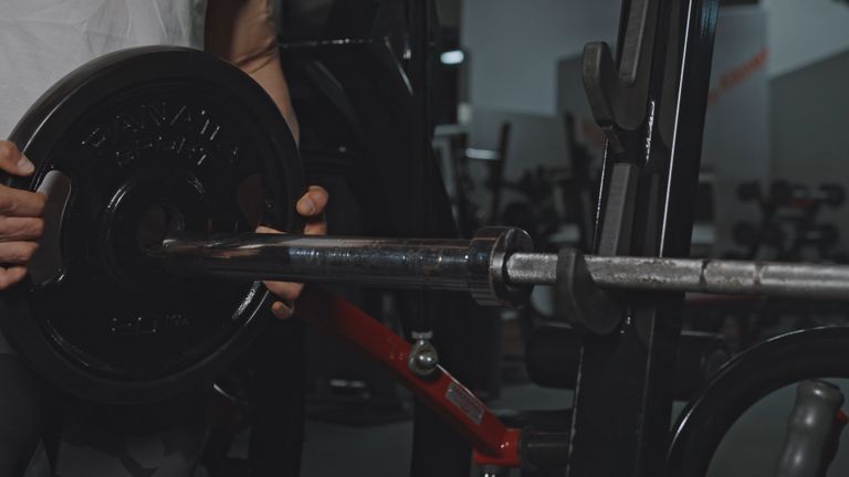 Lifter sliding a weight plate onto a loaded barbell in a dark gym