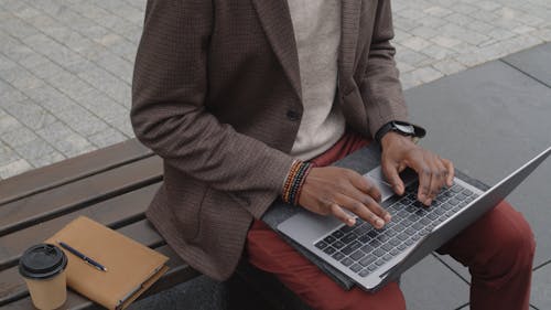 Man Sitting on a Bench while Typing on Laptop