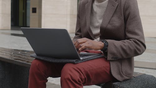 Man Sitting Outside of a Building and Working on Laptop