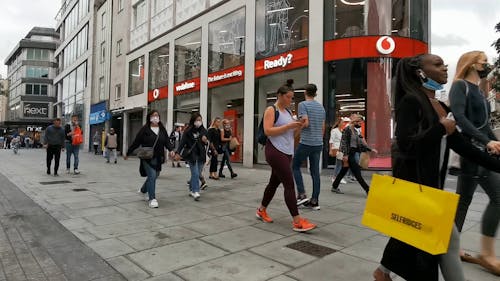 People Walking on Pavement Near Vodafone Store