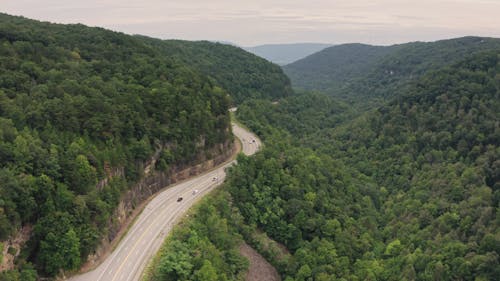 Drone Footage Vehicles Traveling on a Curvy Road Beside the Mountain