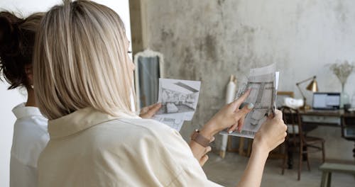 Two Women Looking At Drawings And Comparing Them