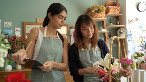 Woman Arranging Flower Basket and Other Woman making Checklist