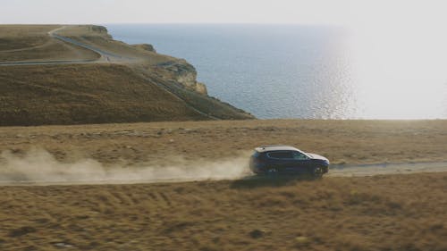 Aerial View of Car Driving Along Coastal Road