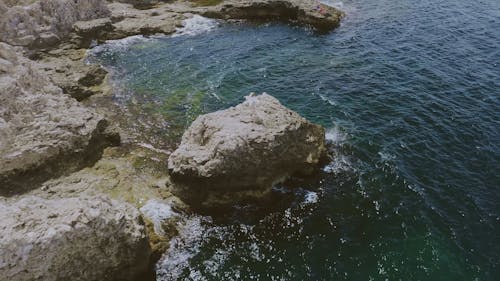 Aerial View of a Woman Standing at the Cliff by the Ocean