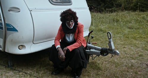 Creepy Clown Smoking Cigarette Sitting next to Trailer