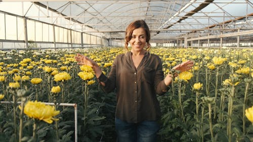 Happy Woman Walking in Greenhouse with Tall Yellow Flowers