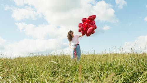 Cheerful Young Woman with Bunch of Red Heart Shaped Balloons in the Fields